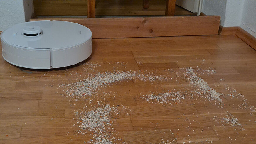 Der Roborock Qrevo Curv 2 Flow saugt auf einem Hartboden Linsen und Haferflocken auf.